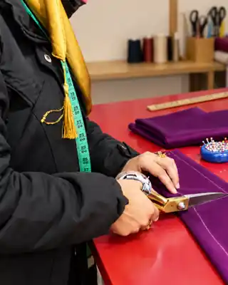 Tailor cutting purple fabric at a worktable, face not visible